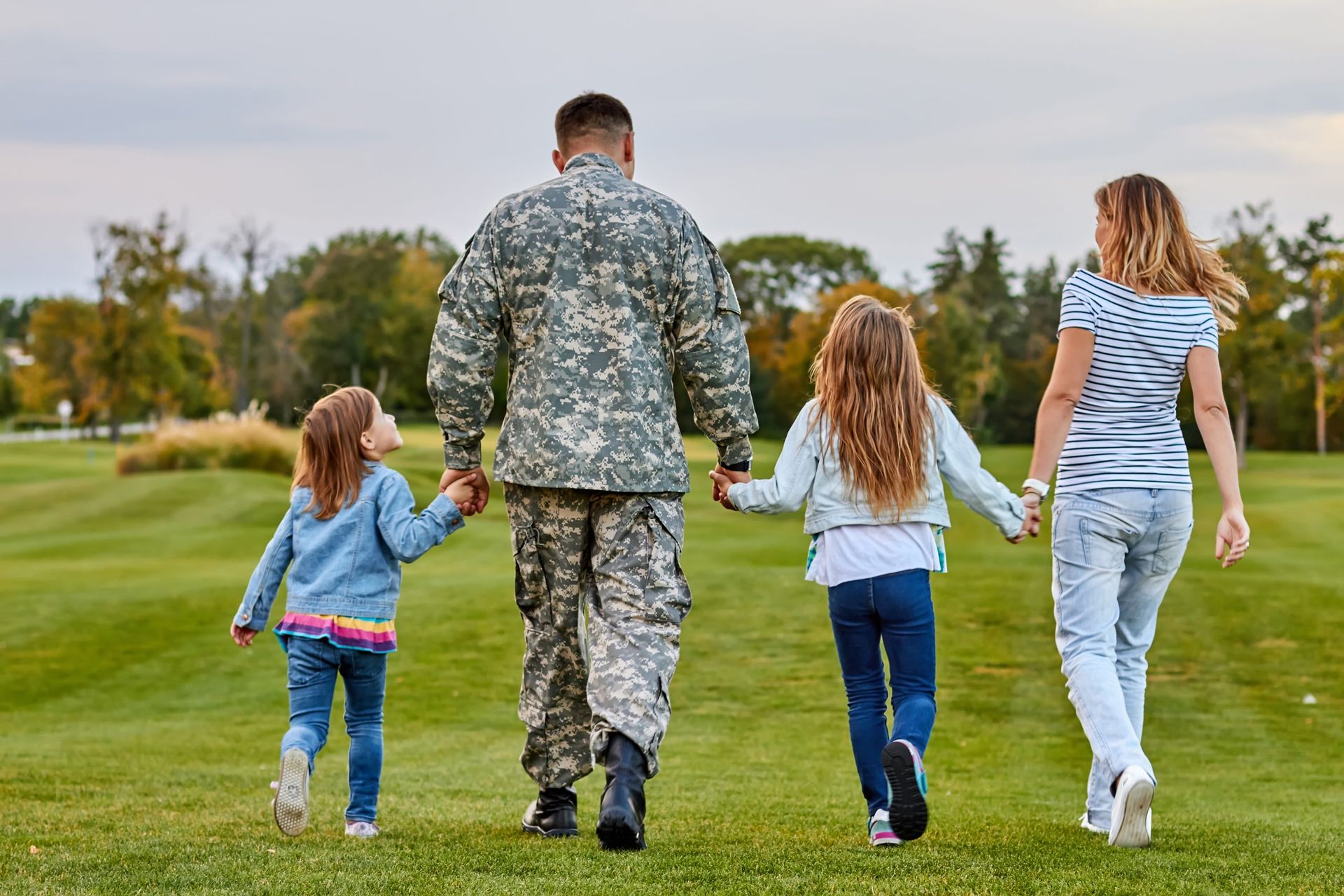military Family walking away across a grassy field, holding hands on a cloudy day