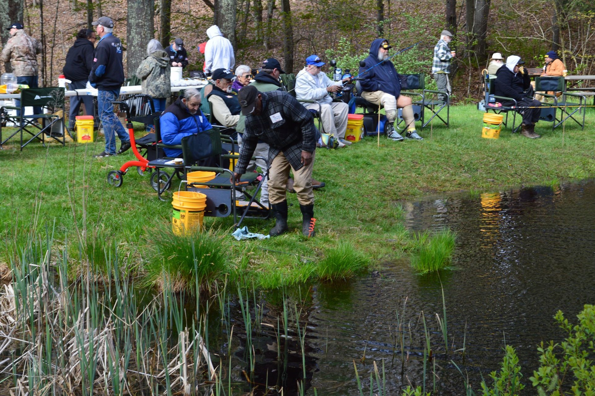 veterans together fishing along a grassy pond bank with gear and buckets on a cloudy day