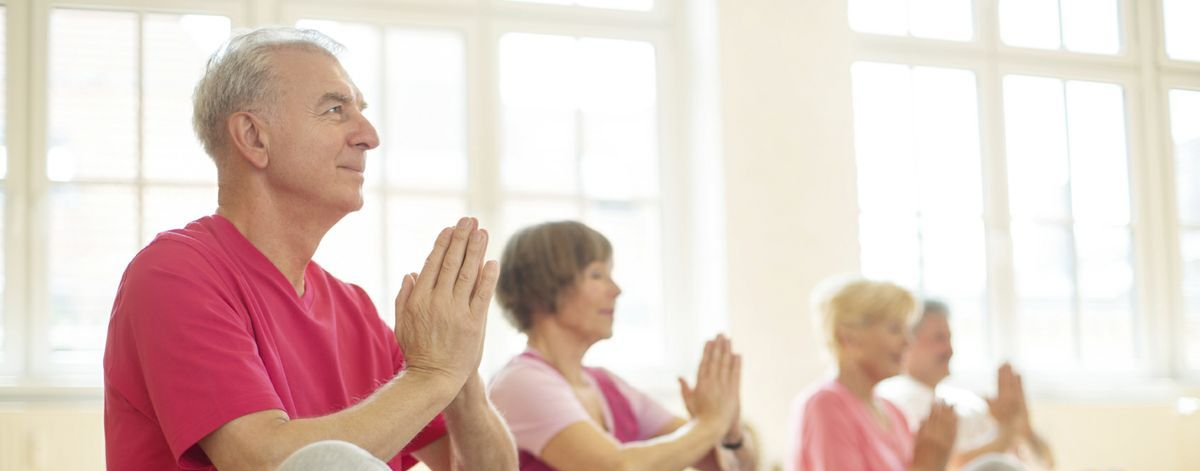 veterans seated in a bright room practicing yoga or meditation, hands together in a prayer pose