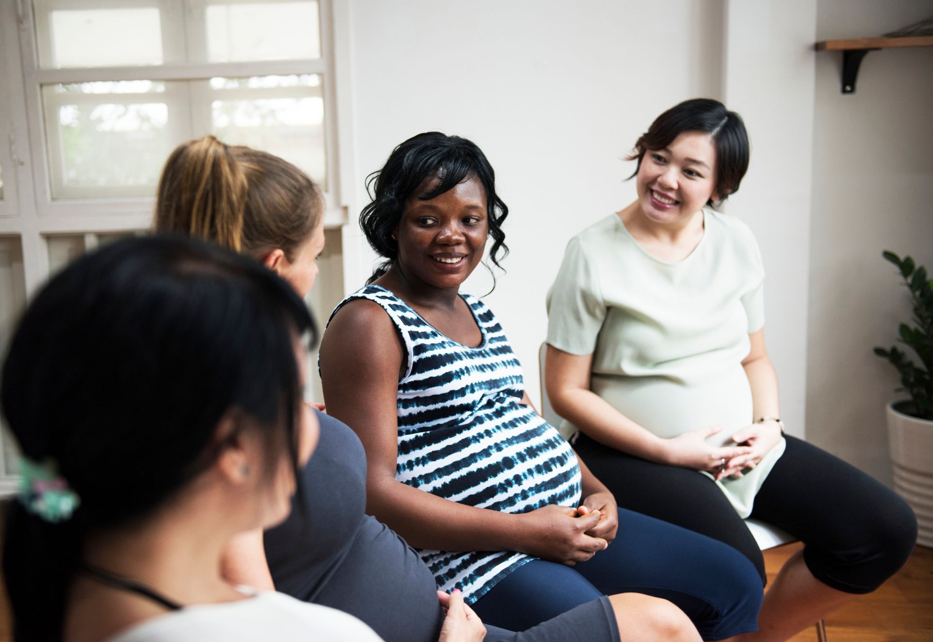 Pregnant women in a circle, smiling and talking in a light-filled room.