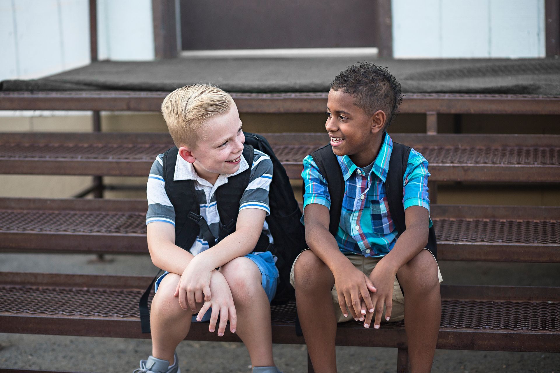 Two boys with backpacks smiling and talking on outdoor steps.