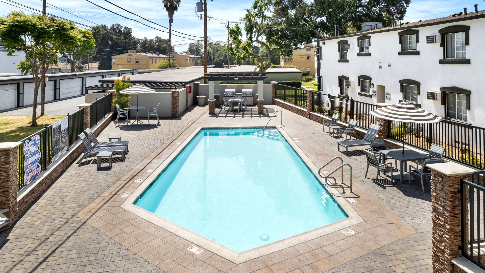 Pool area with pool, tables, and lounge chairs. White building in the background.