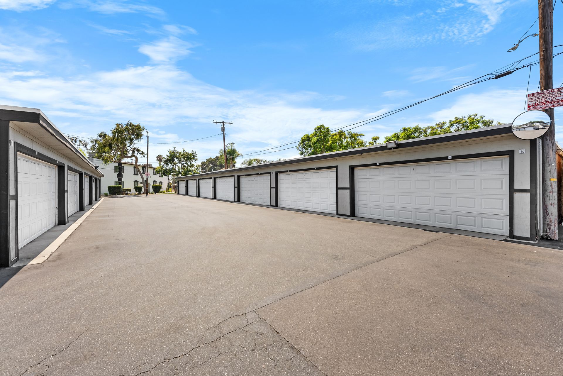 Row of white garage doors with a paved driveway under a blue sky.