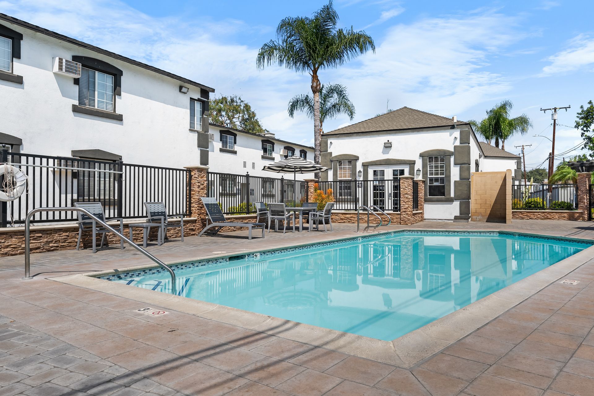 Swimming pool with patio furniture in front of white buildings under a blue sky.