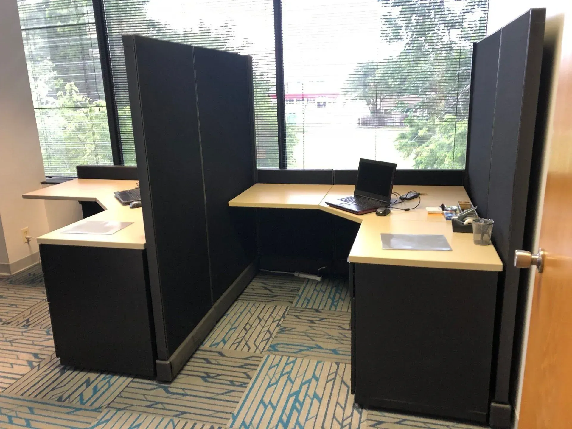 A cubicle with two desks and a laptop on it.
