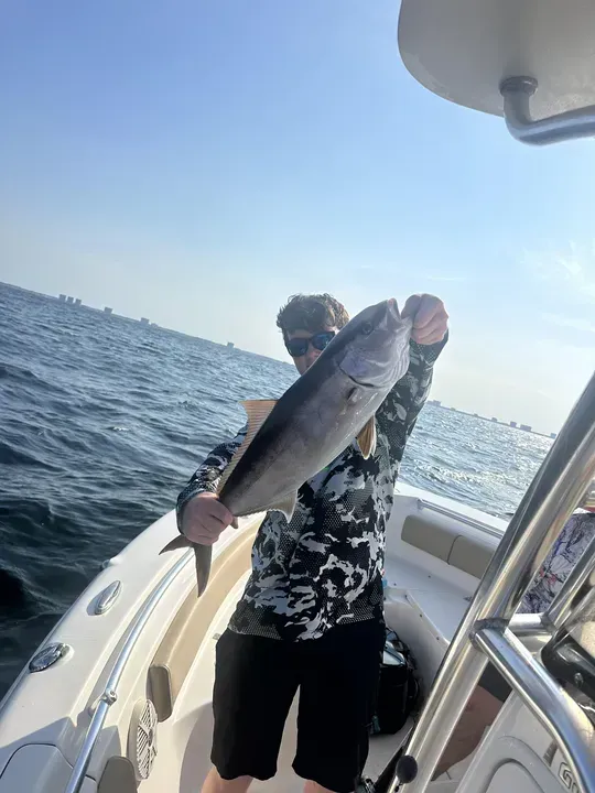 Person on a boat holding a large fish over the deck, with open water and horizon in the background.