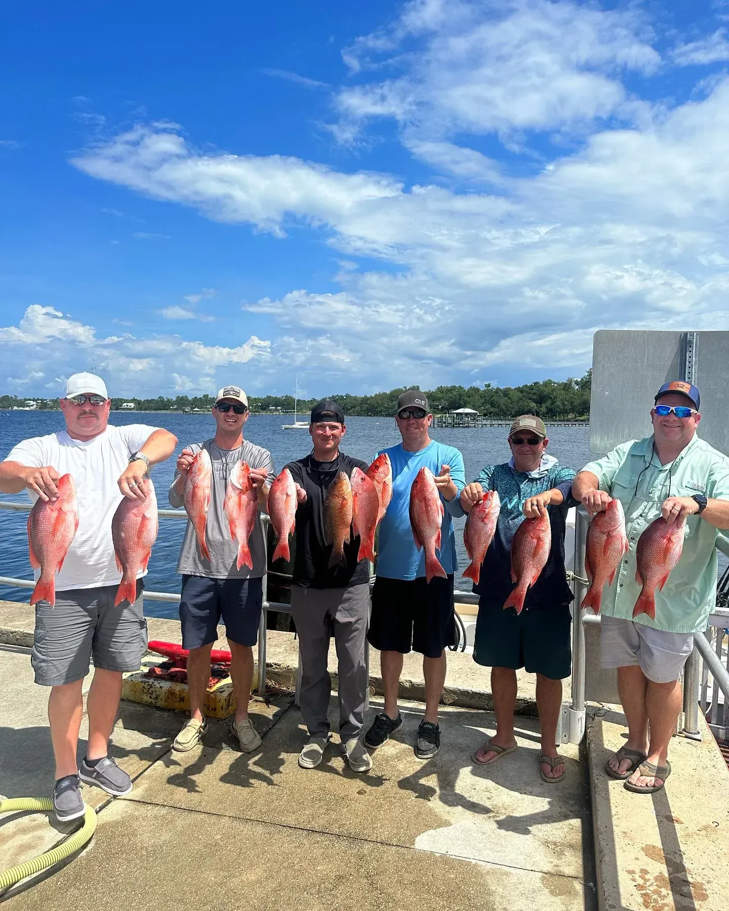 Group of fishermen holding several large fish on a dock under a bright blue sky.