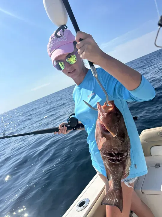 Person on a boat holding up a fish against a blue ocean sky.