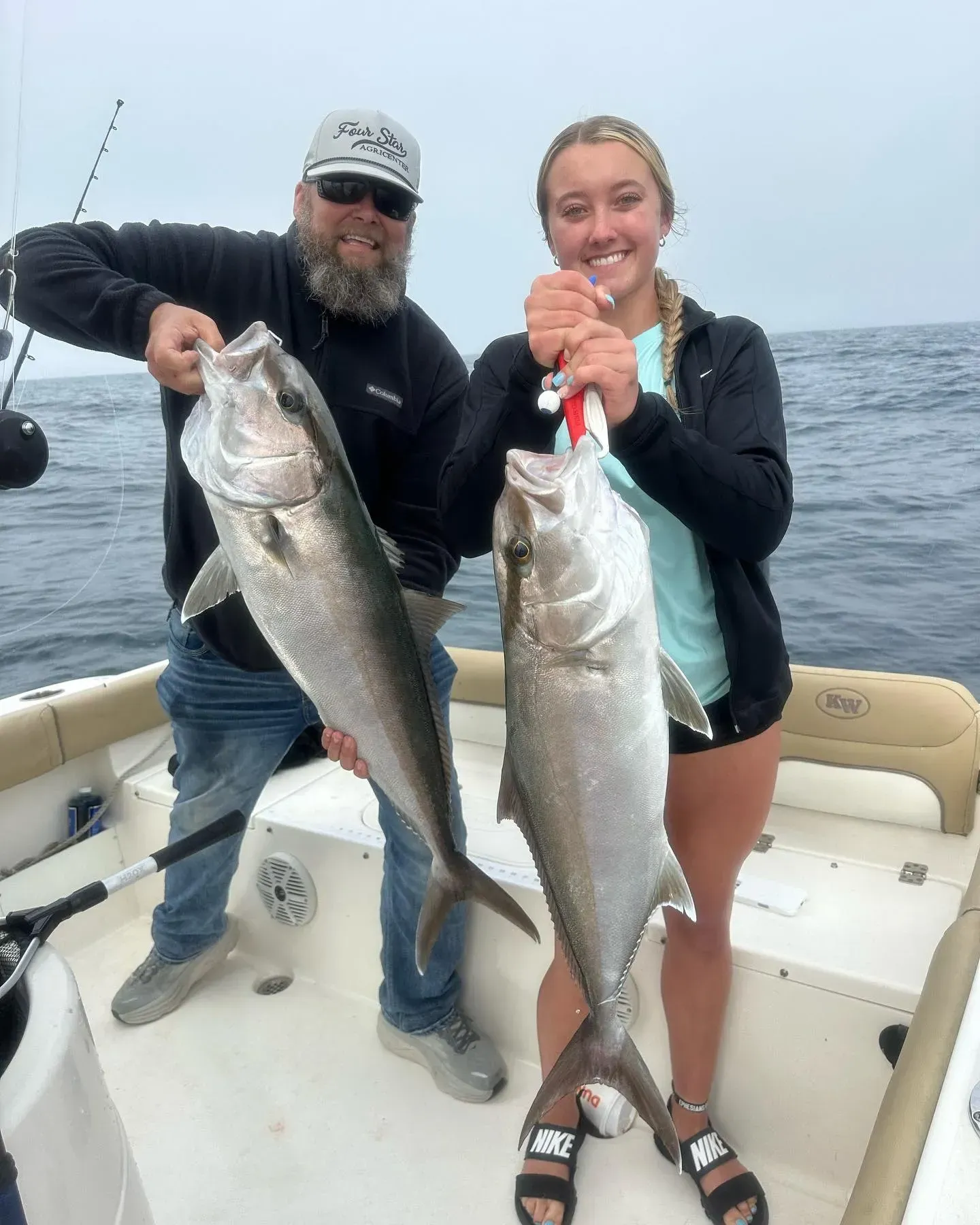Two anglers on a boat hold large fish over open water on a cloudy day