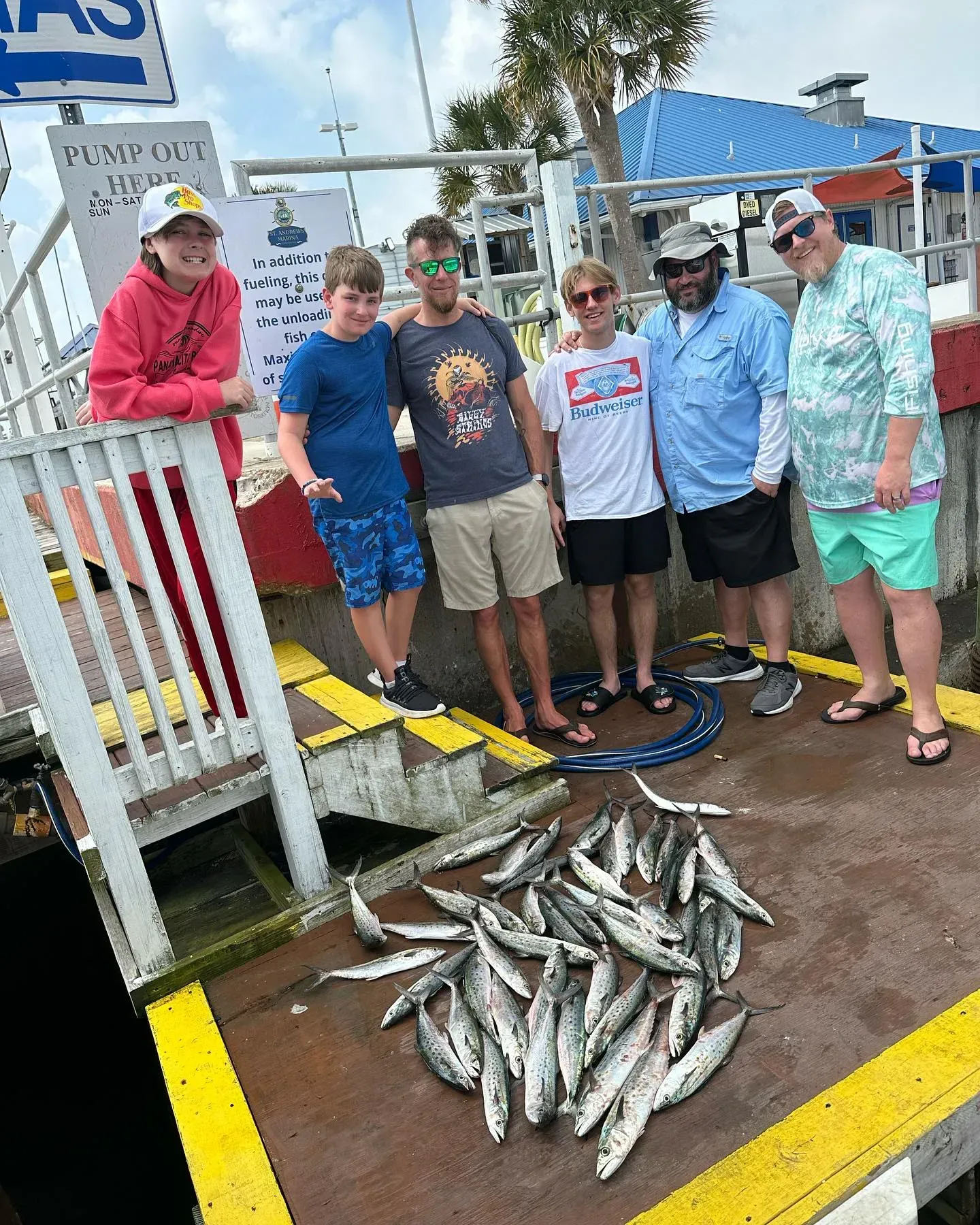 Five people standing by a dock with a large pile of freshly caught fish on the wet ground.