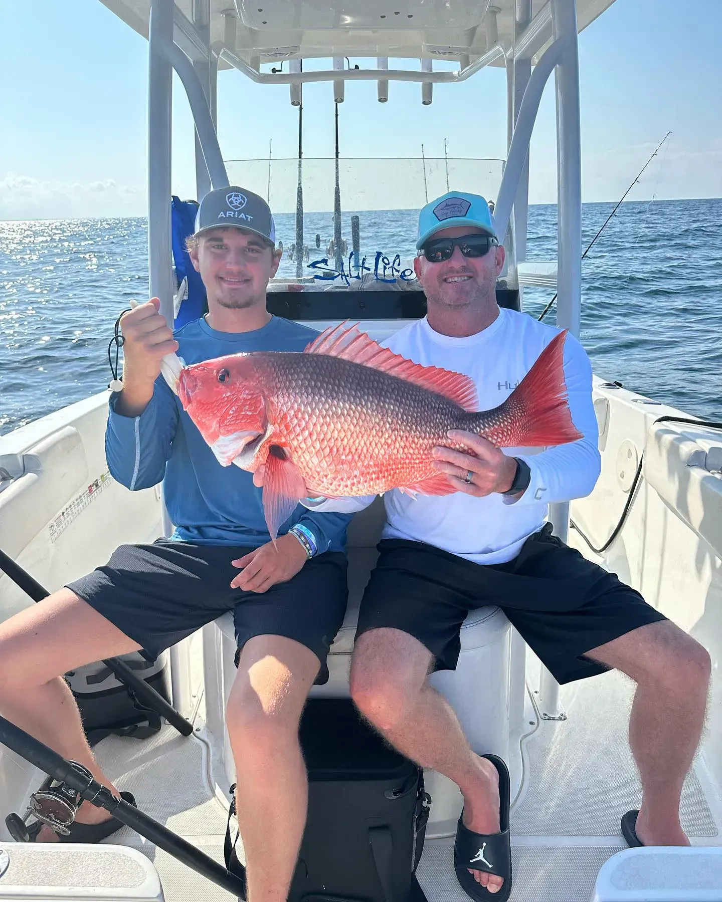Two anglers on a boat hold a large red fish with the ocean behind them.