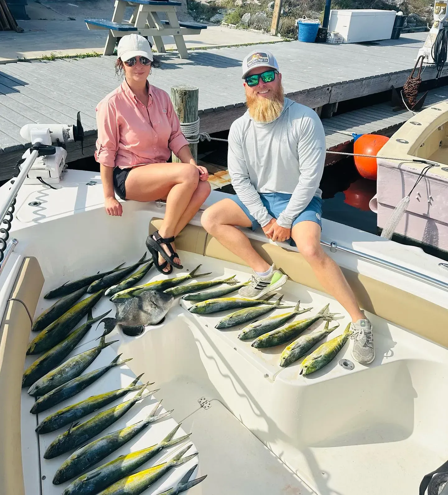Two people sitting on a boat with a large catch of fish spread out on deck