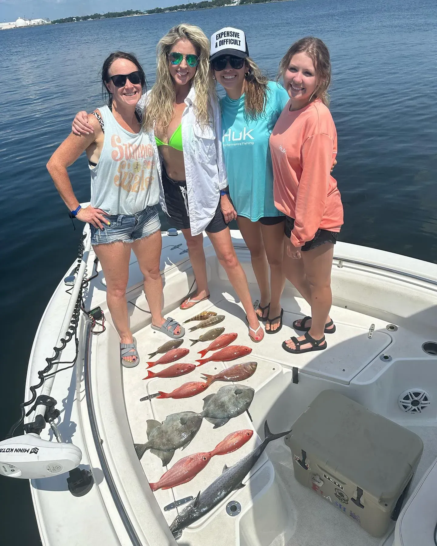 Four people standing on a boat with several fish laid out on the deck, smiling on calm water.