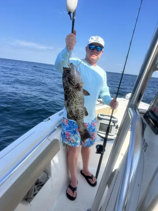 Person on a boat holding up a large fish over the ocean.