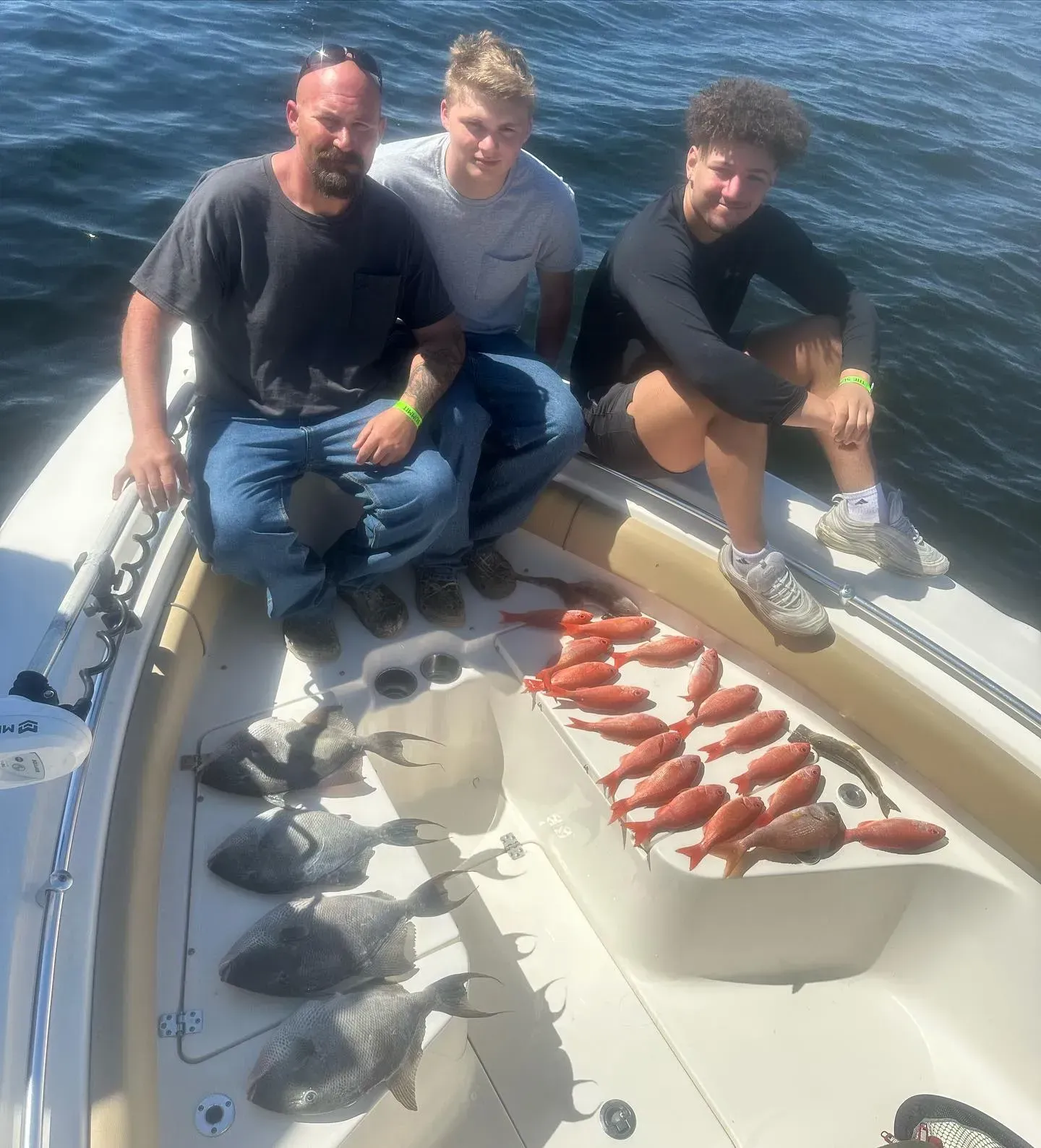 Three people on a boat at sea with a tray of freshly caught fish on deck