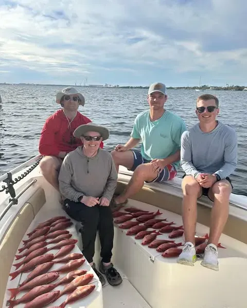 Four people on a boat deck surrounded by rows of freshly caught fish on a sunny day.