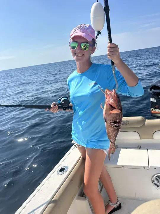Angler on a boat holding a fishing rod and a caught fish on open water under a clear sky