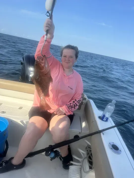 Person holding a large fish on a boat at sea, smiling in a pink shirt