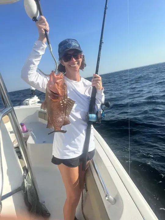 Person on a boat holding up a large fish with the ocean in the background.