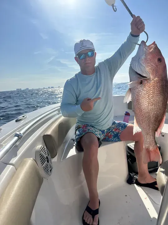 Person on a boat holding a large fish, with ocean and blue sky in the background.