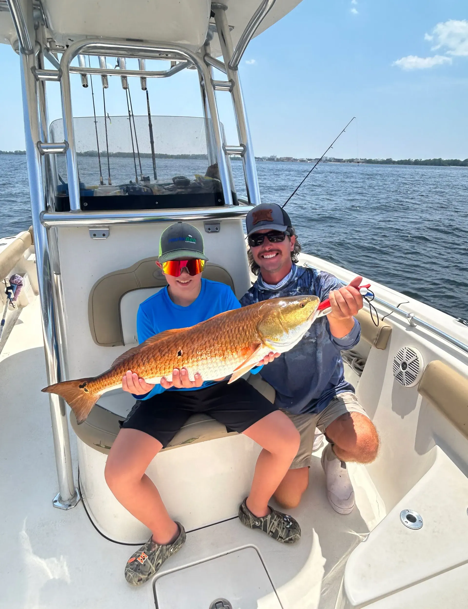 Two people on a boat holding a large fish on a sunny day.