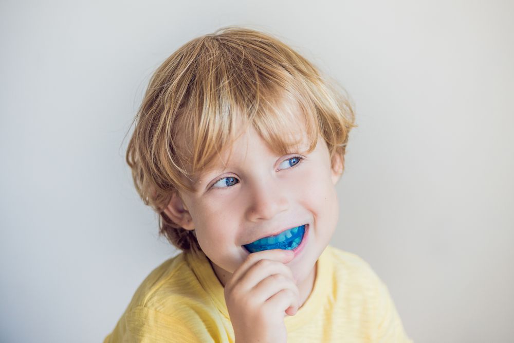 A Young Boy Is Brushing His Teeth With A Blue Mouth Guard — Regal's Dental In Yeppoon, QLD