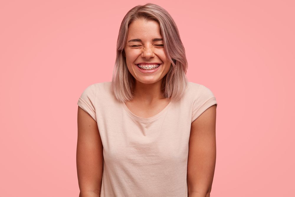 A Woman Is Smiling With Her Eyes Closed On A Pink Background — Regal's Dental In Yeppoon, QLD
