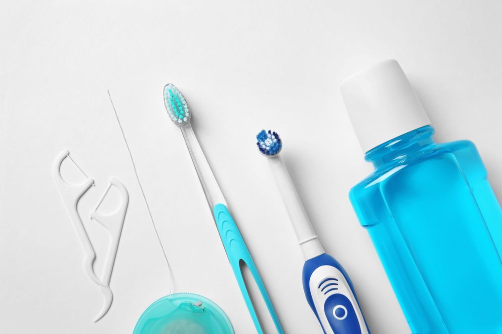 A Toothbrush, Floss, Mouthwash And Toothpaste On A White Surface — Regal's Dental In Yeppoon, QLD