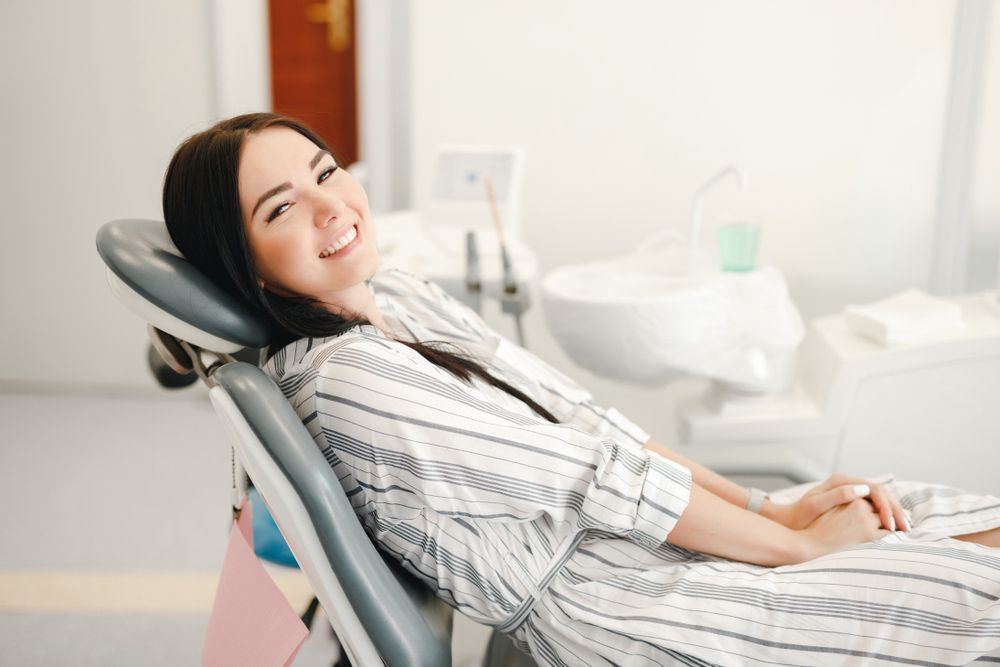 A Woman Is Sitting In A Dental Chair And Smiling — Regal's Dental In Emu Park, QLD