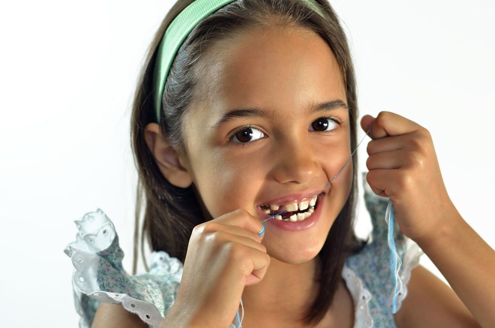 A Little Girl Is Flossing Her Teeth With A Toothpick — Regal's Dental In Yeppoon, QLD