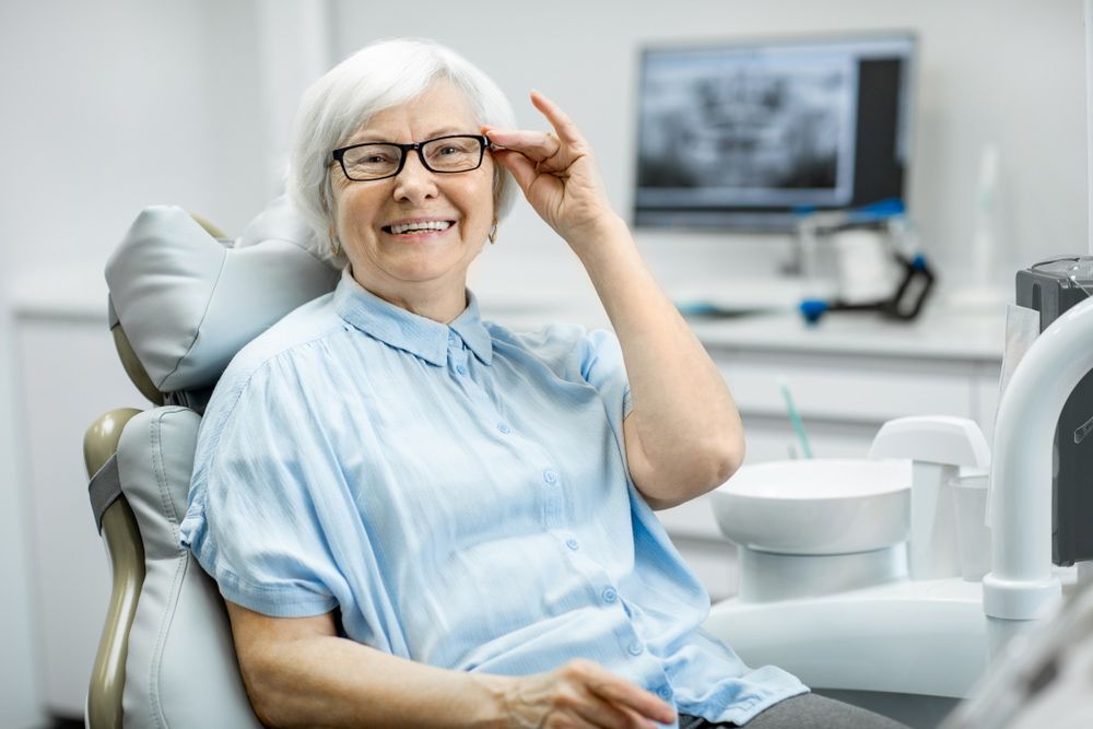 An Elderly Woman Is Sitting In A Dental Chair Adjusting Her Glasses — Regal's Dental In Emu Park, QLD
