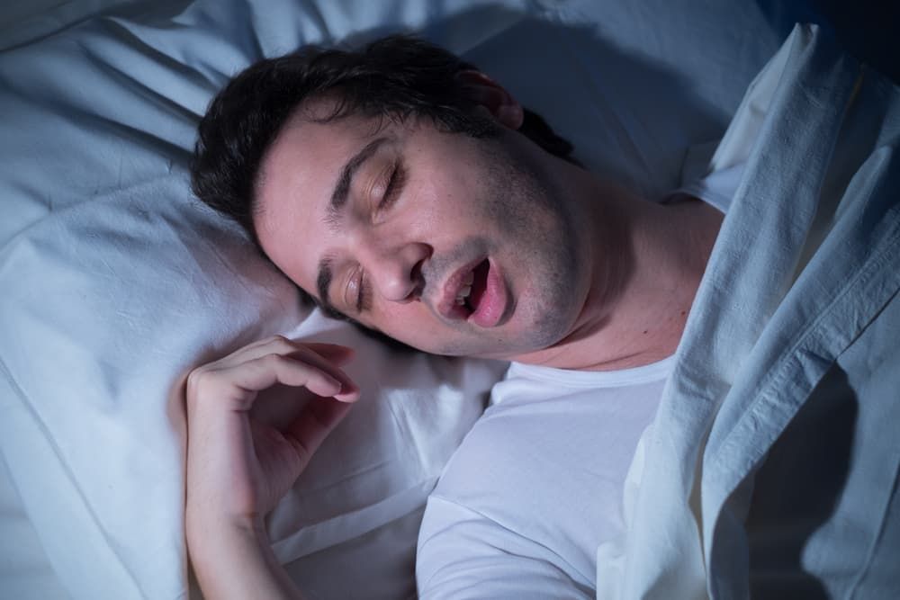 A Man Is Sleeping In A Bed With His Mouth Open — Regal's Dental In Yeppoon, QLD