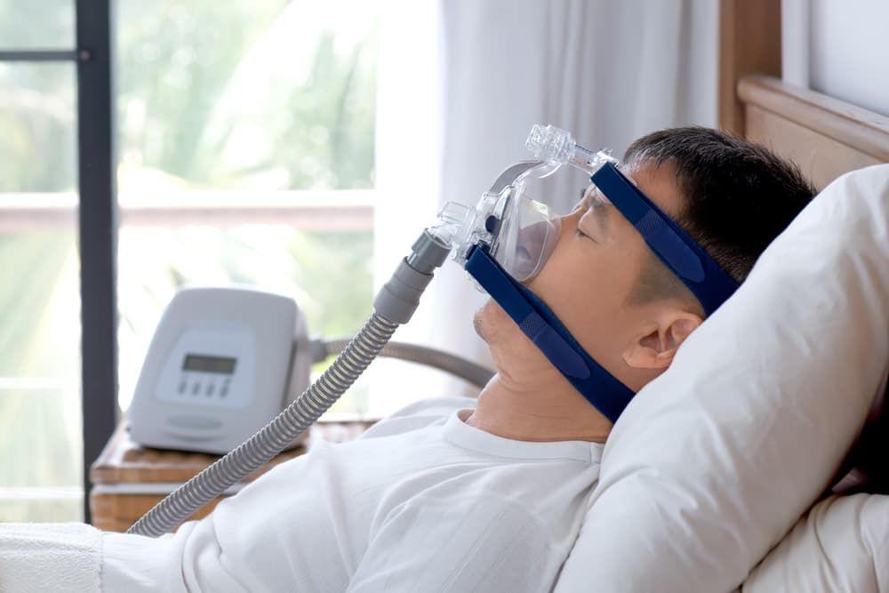 A Man Is Laying In Bed With An Sleeping Mask On His Face — Regal's Dental In Yeppoon, QLD