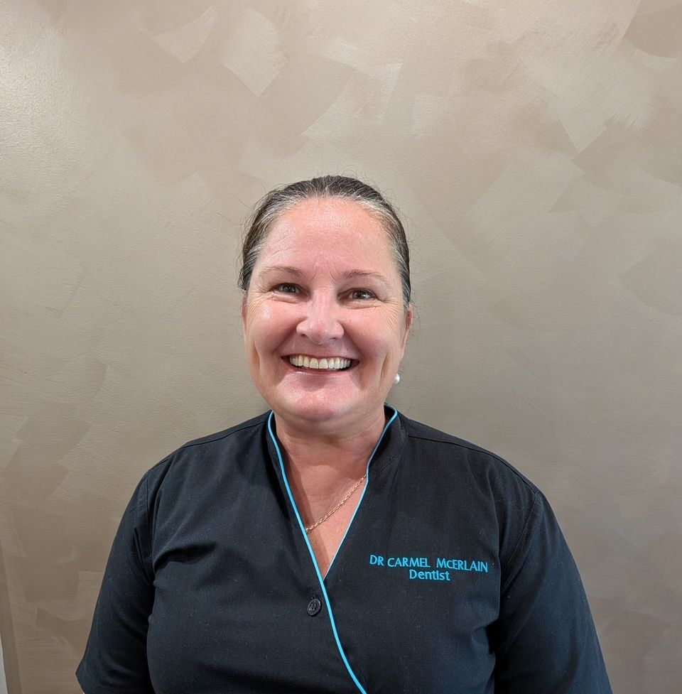 Smiling person in a black uniform shirt with teal trim standing against a beige wall. — Regal's Dental In Yeppoon, QLD