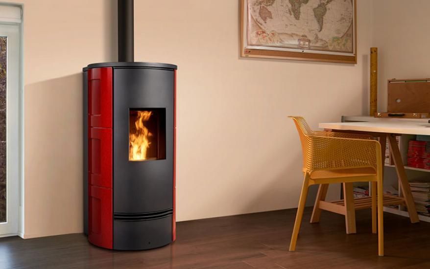 Stufa a legna rossa e nera con fiamma visibile in una stanza moderna accanto a un tavolo da pranzo.