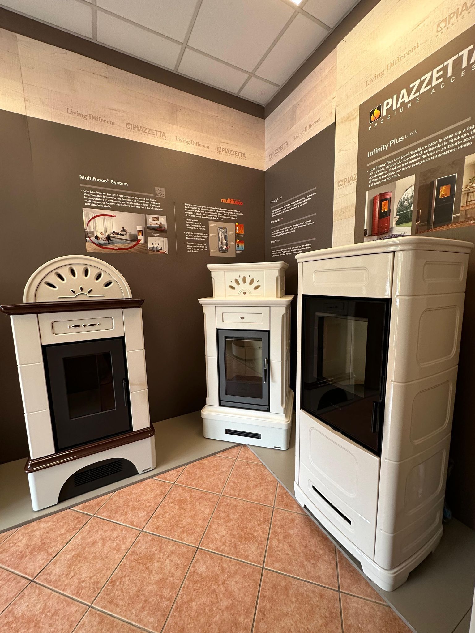 Angolo dello showroom con tre stufe a legna bianche e poster dei prodotti su pareti marroni.