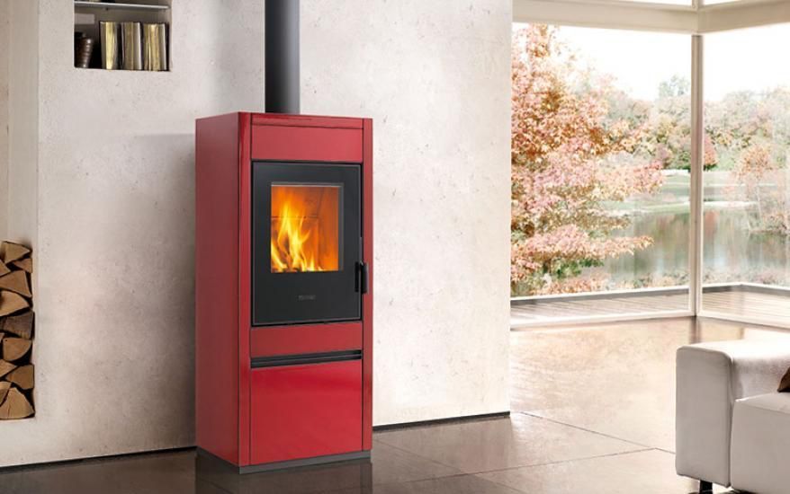 Caminetto moderno rosso con fiamme visibili in un luminoso soggiorno accanto a grandi finestre.