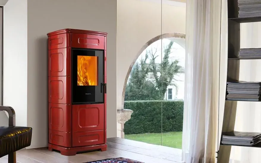 Stufa a legna rossa con fuoco visibile in una stanza luminosa, accanto a una finestra ad arco e una porta aperta.