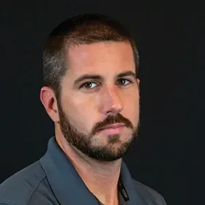 Portrait of a bearded man in a dark collared shirt against a black background