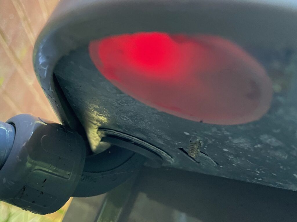 Close-up of a black device underside with a glowing red light and a wheel joint on the left.