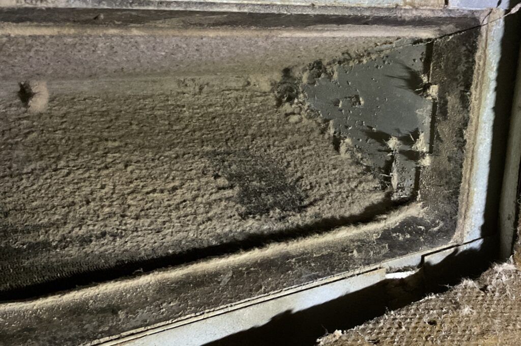 Dusty, damaged window screen or vent frame with torn mesh and dirt buildup