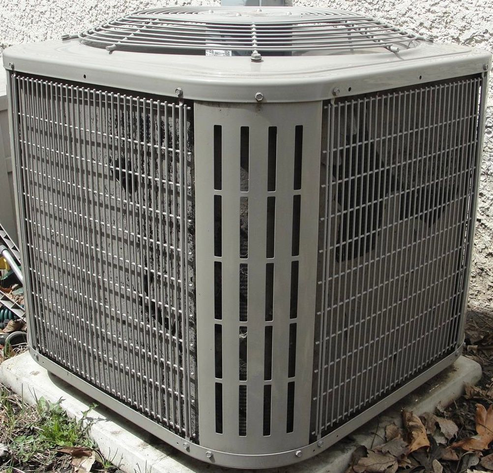 Gray outdoor air conditioner unit with metal grille on a concrete pad