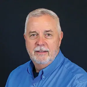 Head-and-shoulders portrait of a man in a blue shirt against a dark background