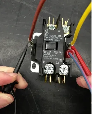 Hand holding a black relay with red, yellow, and blue wires connected on a workbench
