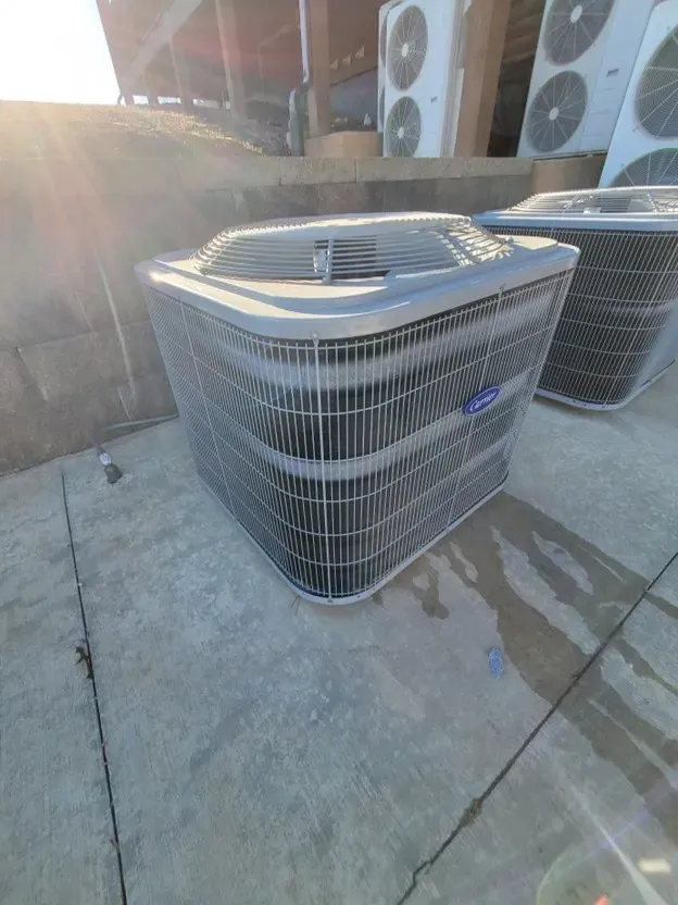 Outdoor air conditioning units on a concrete pad beside a building, with sunlight glare.