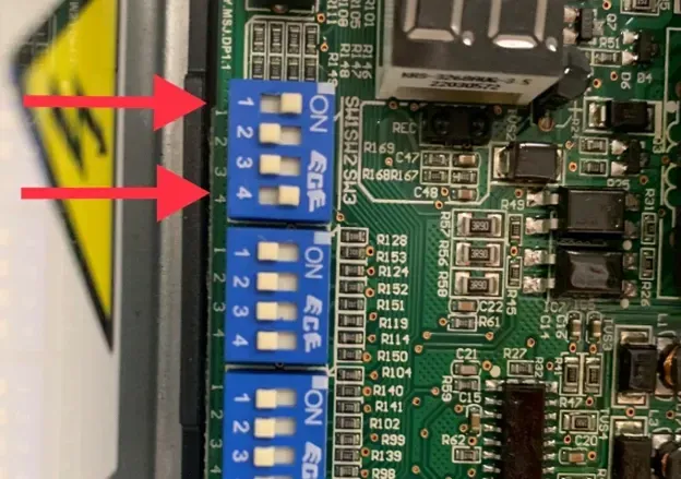 Close-up of blue DIP switches on a green circuit board, with two red arrows pointing at them
