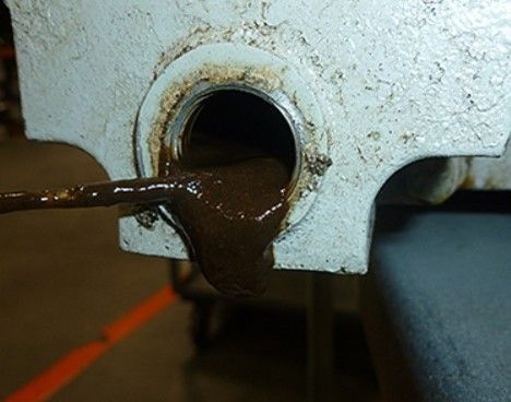 Dark brown liquid leaking from a circular hole in a metal surface