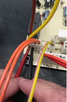 Close-up of hands plugging orange and yellow wires into a small electrical terminal block.