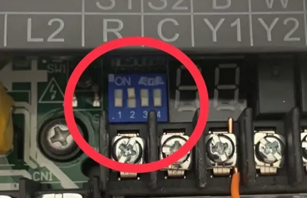 Close-up of a blue DIP switch on an electrical terminal block, circled in red.