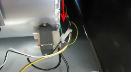 Close-up of electrical wiring and a gray component inside a metal enclosure, with a red arrow pointing to a connector.